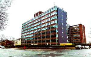 Un grand bâtiment avec des voitures garées devant lui dans l'établissement Fabulous one bedroom apartment near Old Trafford Stadium, à Manchester