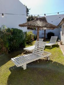 2 sillones blancos y una sombrilla de paja en Sur Hotel en Necochea