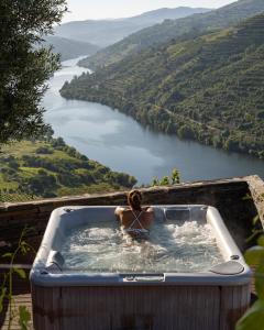 a woman in a hot tub overlooking a river at Imaginário D'El Rei - Guest House in Mesão Frio