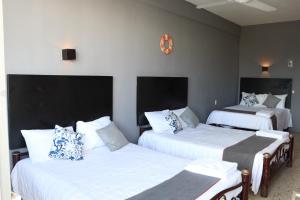Habitación con 3 camas, sábanas blancas y reloj. en Hotel Las Brisas, en Catemaco
