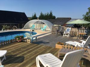 una terraza con sillas blancas y una piscina en Le Bois Gautier en Savigny-le-Vieux