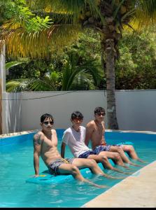 Trzech mężczyzn siedzących na desce surfingowej w basenie w obiekcie Departamento cómodo y hermoso a mts de la playa w mieście San Crisanto