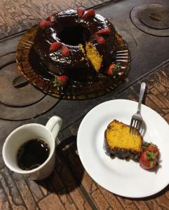 um pedaço de bolo em um prato com um garfo e uma xícara de café em Pousada do Zezé em Bueno Brandão