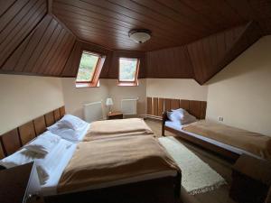 two beds in a room with wooden ceilings and windows at Belle-Aire Vendégház Mátraszentlászló in Mátraszentimre