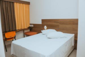 a bedroom with a white bed and a orange chair at Hotel e Pousada Bem Bom - Itu in Itu