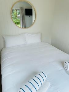 a white bed with a round mirror above it at Athenree Hot Springs & Holiday Park in Waihi Beach