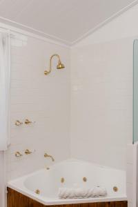 een witte badkamer met een bad en gouden kranen bij Amberesque B&B in Rutherglen
