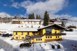 una casa amarilla en la nieve con un coche en Haus Wasserbauer, en Mühlbach am Hochkönig
