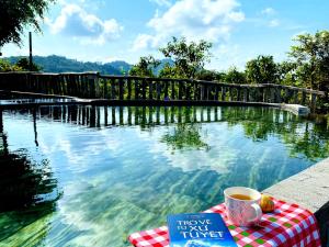 a book and a cup of coffee next to a swimming pool at Floor river view in Cat Tien