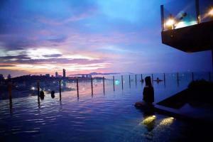 een persoon die op de rand van een waterlichaam zit bij Pattaya Beach Sea View Rooftop Pool Resort in Pattaya