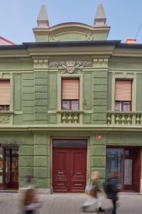 two people walking past a green building with red doors at FERN apartments in Maribor