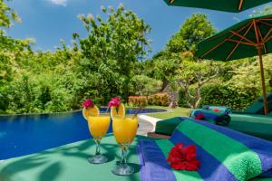 two glasses of orange juice on a table next to a pool at Alamanda Lovina Resort in Lovina