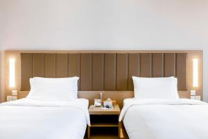 2 bedden in een hotelkamer met witte lakens bij JI Hotel Shanghai Songjiang Sports Center in Songjiang