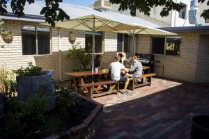 3 persone sedute su un tavolo da picnic sotto un ombrello di Shiralee Hostel -note - Valid passport required to check in a Perth