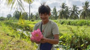 un hombre sosteniendo una flor rosa en un campo en Coco Happy Farm en Ben Tre