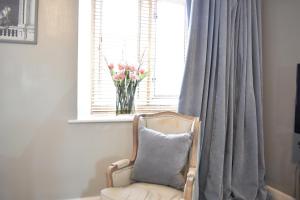 una silla con una almohada en una ventana con un jarrón de flores en Davenford Cotswold Gardens en Stow on the Wold