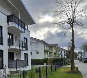 ein weißes Gebäude mit Balkonen und einem Baum auf einer Straße in der Unterkunft Ferienwohnung am Rhododendronpark, 300 m zum Strand in Graal-Müritz