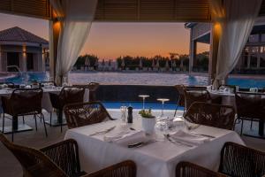 ein Restaurant mit weißen Tischen und Stühlen sowie einem Pool in der Unterkunft Atlantica Mare Village Ayia Napa in Ayia Napa