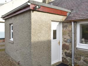 Cette petite maison dispose d'une porte blanche et d'une fenêtre. dans l'établissement Rinnes Cottage, à Aberlour