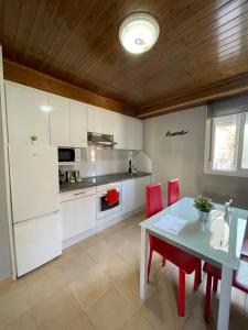 a kitchen with white cabinets and a table and red chairs at Casa Amoedo in Redondela
