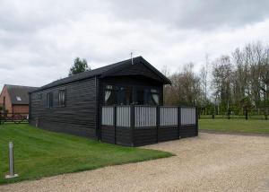 a black cabin with a fence in a field at King Richards Country Lodges in Earl Shilton
