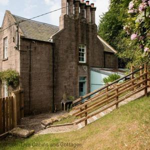 uma velha casa de tijolos com uma cerca de madeira em frente em North Lodge & River Cabin em Banchory