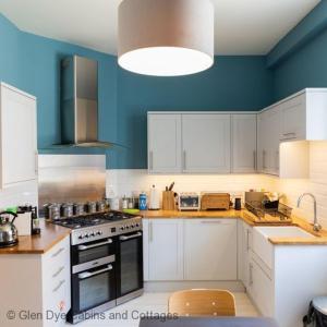 uma cozinha com armários brancos e uma parede azul em North Lodge & River Cabin em Banchory