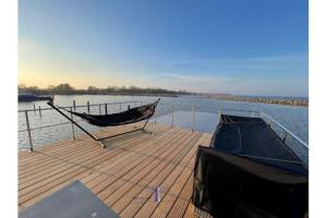 a dock with a hammock and a boat on the water at Hausboot Fjord HAVEN mit Biosauna in Barth in Barth