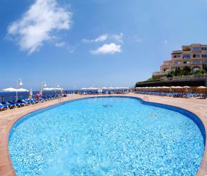 a large swimming pool next to a beach with chairs at Invisa Hotel Club Cala Verde in Es Figueral Beach