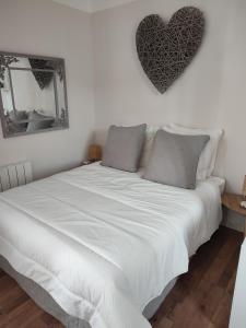 een bed met witte lakens en een hart aan de muur bij Appartement au bord du lac in Bagnoles de l'Orne