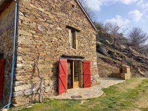 a stone building with red doors and a stone wall at Petite bergerie en pierres tout confort in Salles-Curan