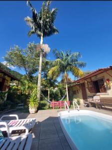 uma piscina com cadeiras e uma palmeira e uma casa em Sítio e Pousada Recanto Dos Ipês em Teresópolis