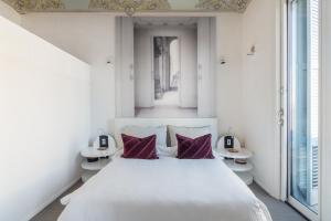 a white bedroom with a large white bed with purple pillows at El Palauet Royal Suites in Barcelona