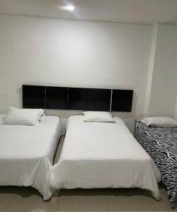 a bedroom with two beds with white sheets and a headboard at Hotel Barrancabermeja Plaza in Barrancabermeja