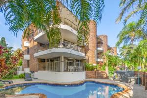 a building with a swimming pool and palm trees at Fuller Holidays-Unit Pacific in Byron Bay