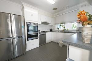una cocina con armarios blancos y electrodomésticos de acero inoxidable en Pet-friendly Bayside 4BR Rental House near Mentone en Parkdale