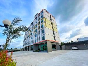 a tall white and yellow building with a palm tree at AT Apartment in Hat Yai