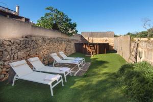 3 chaises blanches assises sur l'herbe à côté d'un mur de pierre dans l'établissement Casa La Limonera. Townhouse with pool for up to 6 persons in Santanyi, à Santanyí