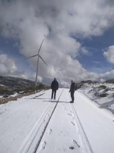 two people walking down a snow covered road with a wind turbine at Las Henrenes 
