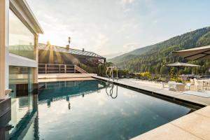 a swimming pool in front of a building with a mountain at Hotel Ravelli Luxury Spa in Mezzana