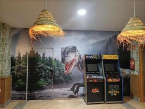 a mural of a dinosaur on a wall with two slot machines at Hostal San Marcos in San Martín de la Vega
