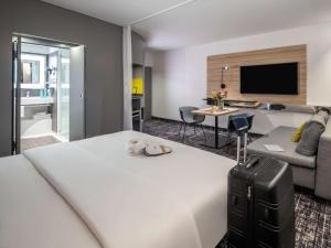 ウィーンにあるNovotel Suites Wien City Donauの白いベッドとリビングルームが備わるホテルルームです。