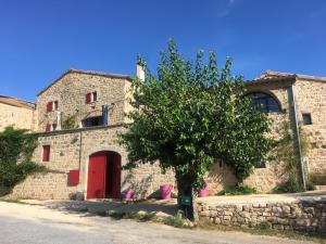 a stone building with a red door and a tree at Le Pressoir De La Deveze in Vernon