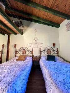 1 dormitorio con 2 camas con sábanas azules y lámpara de araña en Casa Rural Juan de Austria, en Cuacos de Yuste