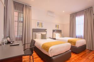 プレトリアにあるTHE Pretoria Hotelのベッド2台とデスクが備わるホテルルームです。