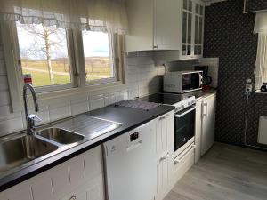 kuchnia z białymi szafkami, zlewem i kuchenką mikrofalową w obiekcie Cottage Båstad/Bjäre w mieście Båstad