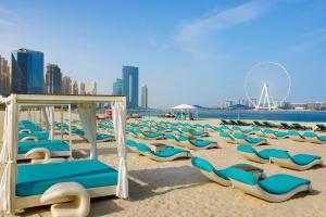 a beach with lounge chairs and a ferris wheel at Habtoor Grand Resort, Autograph Collection in Dubai