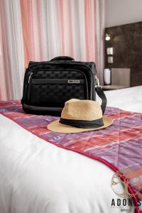un chapeau assis sur un lit à côté d'une valise dans l'établissement Adonis Gapotel, à Gap