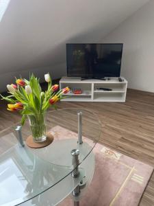 a living room with a tv and a glass table with flowers at Ferienwohnung Fam. Albert in Heuchelheim-Klingen