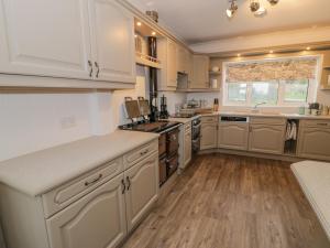 a kitchen with white cabinets and wooden floors and a window at Cynefin in Llandyfrydog